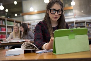 Junge Studentin vor einem iPad in einer Bibliothek.